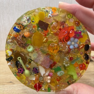 A yellow coloured picky pad in a circle shape. The sensory toy contains a variety of beads, charms, and other embellishments.