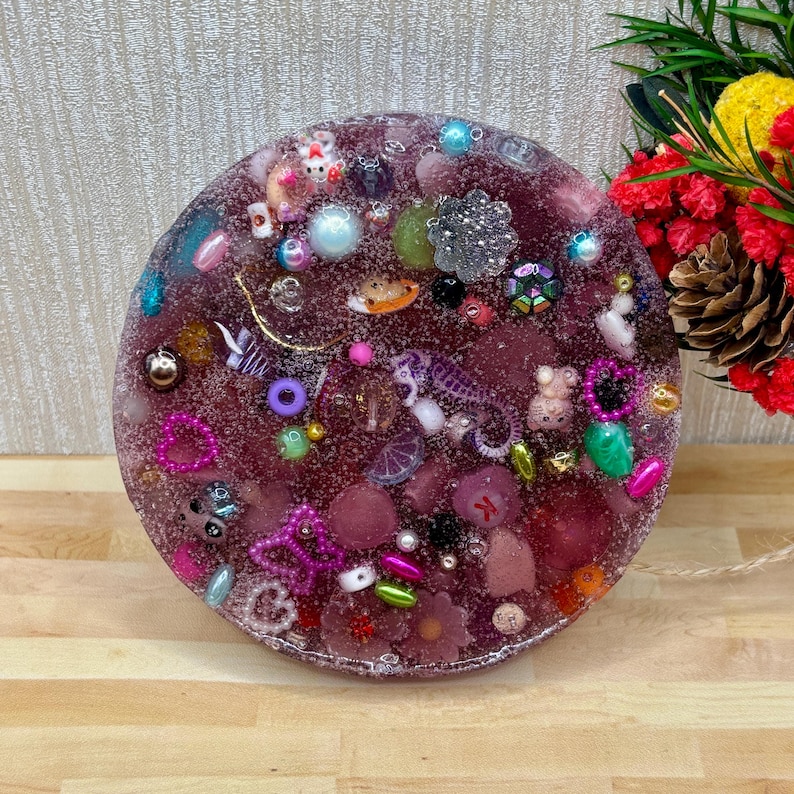 A circle shaped picky pad. The colour is purple. It is made from a reusable material and includes beads, charms, flatbacks and other embellishments.