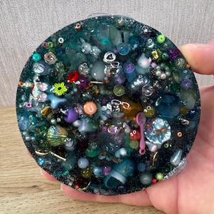 A circle shaped picky pad. The colour is blue. It is made from a reusable material and includes beads, charms, flatbacks and other embellishments.
