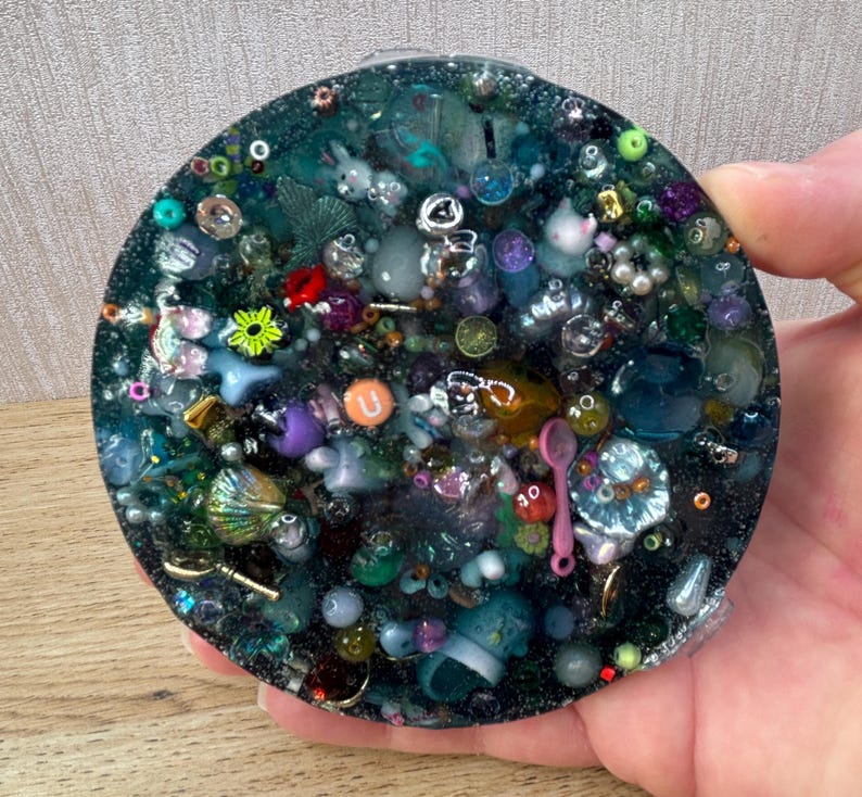A circle shaped picky pad. The colour is blue. It is made from a reusable material and includes beads, charms, flatbacks and other embellishments.