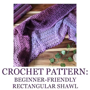 Può includere: Uno scialle all'uncinetto fatto a mano in tonalità viola, dal viola scuro al lavanda chiaro. Lo scialle è drappeggiato su una superficie di legno, con libri e verde sullo sfondo. Il testo in basso recita "CROCHET PATTERN: BEGINNER-FRIENDLY RECTANGULAR SHAWL."