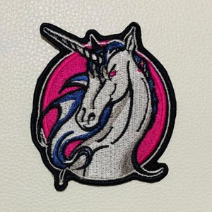 May include: A white unicorn with a blue mane and tail, against a pink background. The unicorn has a single horn and a red eye. The patch is embroidered and has a black outline.