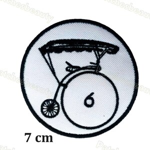 Może przedstawiać: Okrągła naszywka z czarno-białą ilustracją zabytkowego roweru penny-farthing. Liczba 6 jest widoczna na dużym kole. Naszywka ma średnicę 7 cm.