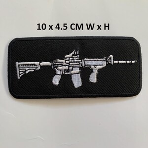 Könnte beinhalten: Schwarzer rechteckiger Aufnäher mit einem weiß-grauen, gestickten Gewehrmotiv. Der Aufnäher misst 10 x 4,5 cm, mit den Abmessungen darüber gedruckt.