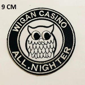 Op de afbeelding: Een geborduurde patch in zwart en wit met een witte uil in het midden. De uil heeft grote ogen en een rond lichaam. De patch is omgeven door een zwarte cirkel met de tekst "Wigan Casino All Nighter" in wit.