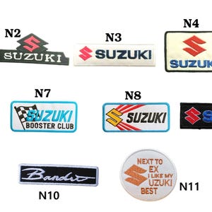 May include: A collection of eleven embroidered patches featuring the Suzuki logo and text. The patches vary in shape and color, including green, black, white, and yellow. Some patches include the word "Bandit" and "Booster Club".