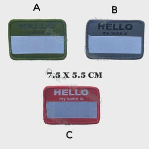 Puede incluir: Tres parches rectangulares para etiquetas de nombre. Uno es verde oliva con "HELLO" en la parte superior. El segundo es gris con "HELLO my name is". El tercero es rojo con "HELLO my name is". Cada parche tiene una sección azul claro para escribir un nombre. Cada parche mide 7,5 x 5,5 cm.