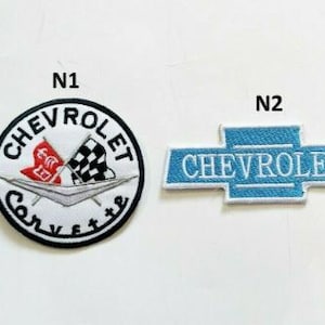 May include: Two embroidered patches featuring the Chevrolet logo. One is a circular patch with the word "Chevrolet" and "Corvette" surrounding a design of flags. The other is a blue bowtie logo with the word "Chevrolet".