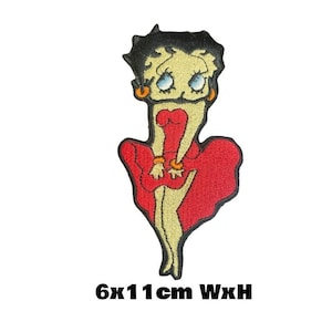 May include: An embroidered iron-on patch featuring a cartoon character in a red dress. The character has black hair, large eyes, and a bright smile. The patch measures 6 cm wide by 11 cm high.