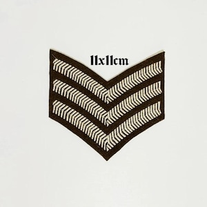May include: A brown and white chevron patch, measuring 11x11cm. The patch features three white chevrons on a dark brown background. The text "11x11cm" is printed above the patch.