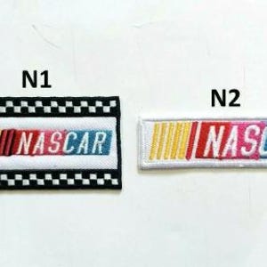 May include: Two embroidered NASCAR patches. One is rectangular with a black and white checkered border, the other is a white rectangle. Both feature the word "NASCAR" in red, pink, and blue.