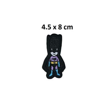 Puede incluir: Parche de hierro bordado en negro y morado de un superhéroe de dibujos animados con una capa y un cinturón amarillo. El parche mide 4,5 x 8 cm.