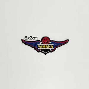 Puede incluir: Un parche bordado azul y rojo con un logotipo de Yamaha y alas. El logotipo es amarillo y el texto dice "Yamaha". El parche mide 8 cm por 3 cm.