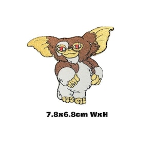 May include: An embroidered iron-on patch featuring a cartoon character with brown fur, large ears, and red eyes. The character is standing with its arms raised and has a white belly. The patch measures 7.8 x 6.8 cm.