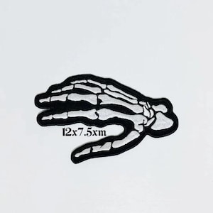 May include: Black and white embroidered patch of a skeleton hand with the text "12x7.5xm".