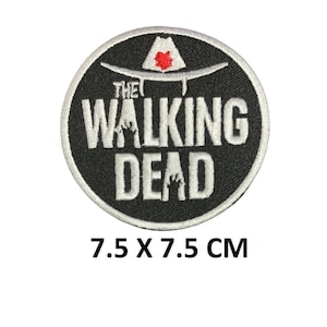 May include: A circular embroidered patch featuring a black background with white text that reads THE WALKING DEAD. Above the text is a white sheriff hat with a red star emblem. The patch measures 2.95 x 2.95 inches as indicated by the text below.