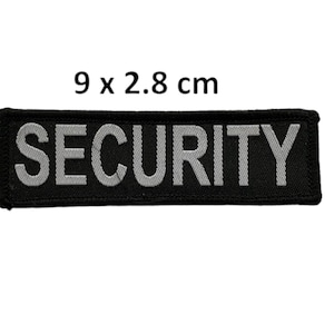 May include: Black fabric patch with the word "SECURITY" in white reflective lettering. The patch measures 9 by 2.8 centimetres.