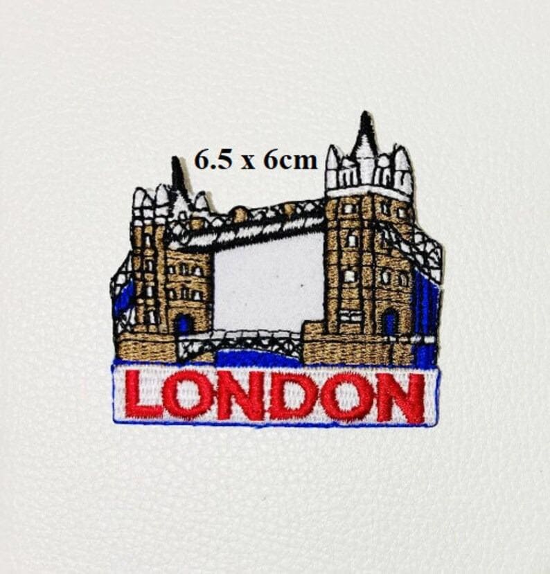 May include: An embroidered patch featuring the Tower Bridge in London, England. The patch is brown, white, and blue with the word "LONDON" in red letters on a blue background. The patch measures 6.5 x 6 cm.