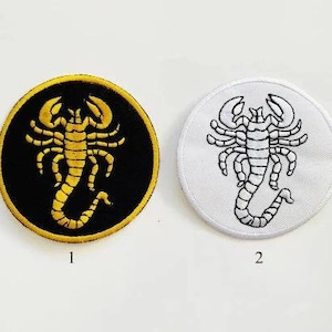 May include: Two circular embroidered patches with scorpion designs. One features a gold scorpion on a black background with a gold border. The other has a black scorpion design on a white background with a white border.