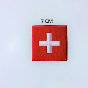May include: A square, red patch with a white cross, measuring 7 cm. The patch has a red border and the text "7 CM" above it. The design is reminiscent of the Swiss flag.