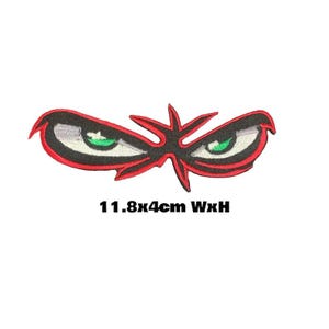 May include: Red and black embroidered patch with two green eyes and a starburst design. The patch measures 11.8 cm wide by 4 cm high.