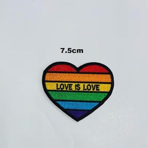 May include: A heart-shaped patch with a rainbow design and the text "LOVE IS LOVE". The patch is approximately 7.5cm in size and has a black border. The colours include red, orange, yellow, green, blue, and purple.