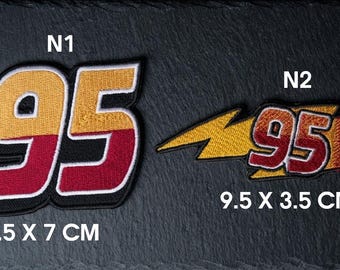 May include: Two embroidered patches featuring the number 95. Patch N1 is 7.5 by 7 cm, colored yellow and red with a black border. Patch N2 is 9.5 by 3.5 cm, featuring the number 95 over a yellow lightning bolt shape with red accents and a black border.