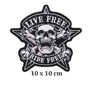 Puede incluir: Parche bordado en blanco y negro con un diseño de calavera y huesos cruzados. El parche tiene forma de estrella y presenta el texto "LIVE FREE" y "RIDE FREE". El parche mide 10 x 10 cm.