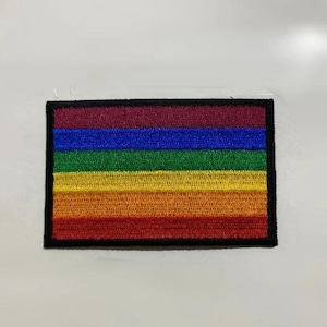 May include: A rainbow pride flag patch with six horizontal stripes in the colors red, orange, yellow, green, blue, and purple. The patch is embroidered and has a black border.