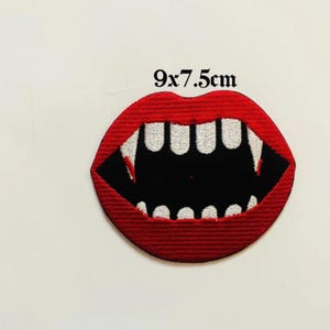 Può includere: Toppa ricamata raffigurante una bocca rossa con zanne affilate e interno nero. Misura 9 x 7,5 cm. Il design è una rappresentazione stilizzata di denti da vampiro, perfetta per aggiungere un tocco spettrale a vestiti o accessori.