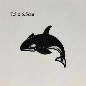 Könnte beinhalten: Schwarzer und weißer gestickter Aufnäher einer Orca, oder Killerwal, mit weißem Bauch. Der Aufnäher misst 7,5 x 6,5 cm.
