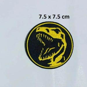 May include: A circular black embroidered patch with a yellow Tyrannosaurus Rex head design. The patch is 7.5 x 7.5 cm, approximately 3 x 3 inches. The text '7.5 x 7.5 cm' is visible.