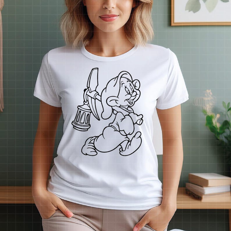 Puede incluir: Camiseta blanca con una ilustraci&oacute;n de dibujos animados en blanco y negro de un personaje sosteniendo un pico y una linterna. El personaje se representa en una pose de carrera. La camiseta tiene cuello redondo y mangas cortas.