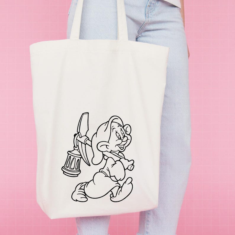 Puede incluir: Bolso tote de color crema con una ilustraci&oacute;n en blanco y negro de un personaje de dibujos animados enano. El enano corre llevando un pico y una linterna. El bolso tiene dos asas.