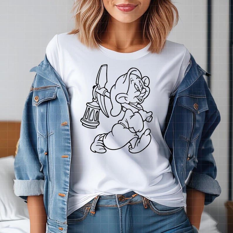 Puede incluir: Camiseta blanca con una ilustraci&oacute;n de dibujos animados en blanco y negro de un personaje enano que lleva un pico y una linterna. El dise&ntilde;o est&aacute; centrado, mostrando un estilo de dibujos animados cl&aacute;sico.