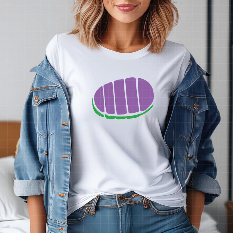 May include: White t-shirt featuring a purple and green graphic design. The design is an oval shape with vertical purple stripes and a green border. The shirt is worn with a blue denim jacket and blue jeans.