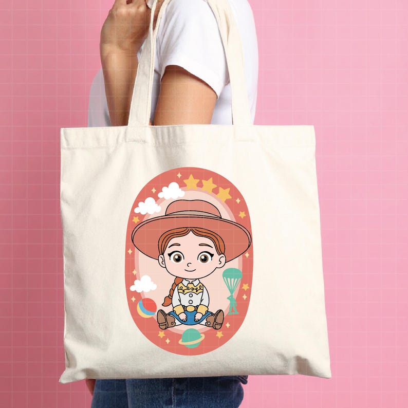 May include: A cream-colored tote bag featuring a cartoon illustration of a cowgirl character. The illustration is set within an oval frame with stars, clouds, and a rainbow. The cowgirl wears a hat, a yellow shirt, and blue jeans.