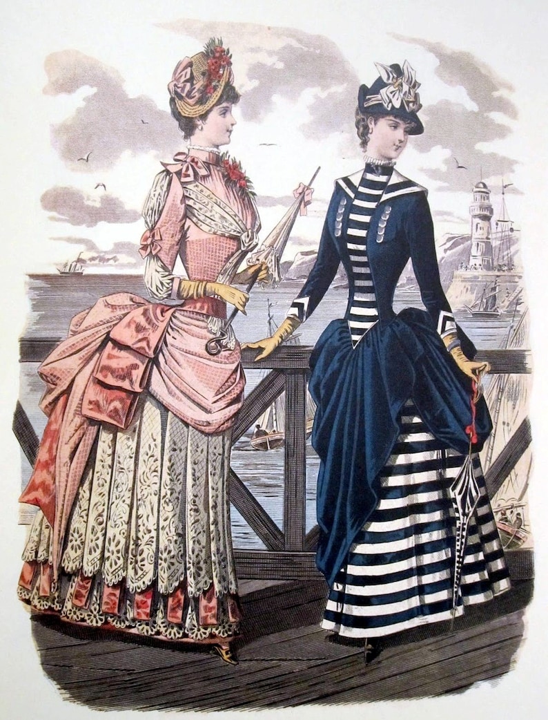 May include: Two women in fashionable 19th-century attire stand on a wooden pier overlooking a harbor. One woman wears a pink and white dress with a lace trim and a large hat with flowers. The other woman wears a navy blue dress with white stripes and a black hat with a white bow.