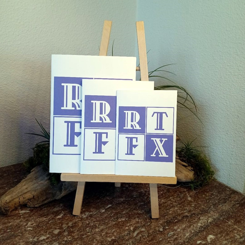 May include: Three white cards with a purple border and white letters on a wooden easel. The cards are different sizes and each has a different letter: R, F, T, and X.