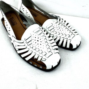 May include: A pair of white leather sandals with a woven design. The sandals have a flat sole and an open toe. The brand name "BASIC" is visible on the insole.