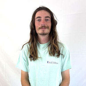 May include: A pale green t-shirt with a small logo on the upper left chest. The shirt is worn with dark blue jeans. The text on the shirt reads "Design Technologies Conference".