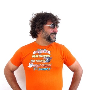 May include: A man wearing an orange t-shirt with the text "This is my Official Gear Jammin Tire Smokin Night Cruisin T-Shirt".