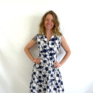 May include: A white dress with a navy blue geometric pattern. The dress has a collared neckline, sleeveless design, and a knee-length skirt.