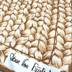 May include: A silk scarf with a woven pattern in shades of brown and beige. The scarf has a brown border and a white label with the signature "Diane Von Furstenberg" in black script.