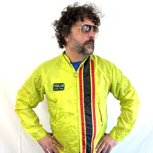 May include: A yellow nylon jacket with a black and red stripe down the front. The jacket has a zipper closure and a  "Poulan Chain Saws" logo on the left chest.