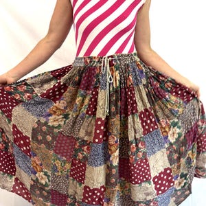 May include: A long, full-length skirt featuring a patchwork design of various fabric patterns, including burgundy with white polka dots, floral prints with roses, and intricate paisley motifs. The skirt has an elastic waistband with a drawstring.