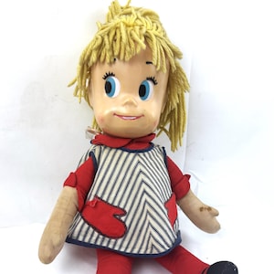 May include: Vintage doll with a painted face, blue eyes, and yellow yarn hair. The doll wears a red top and leggings, a blue and white striped apron, and black shoes. The doll is a classic toy.
