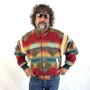 May include: A zip-up fleece jacket featuring a multi-colored geometric pattern in shades of red, teal, yellow, and brown. The jacket has a high collar, long sleeves with solid-colored cuffs, and two front pockets with light-colored trim.