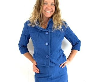 May include: A blue two-piece suit featuring a jacket with three buttons and a matching skirt. The jacket has a unique collar and three-quarter sleeves. The suit is made of a textured fabric and is a solid, vibrant blue color. The skirt is knee-length.