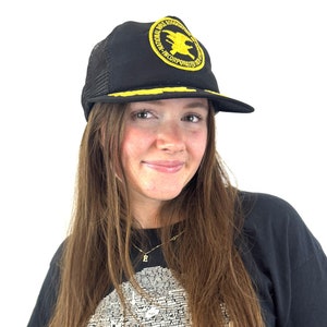 Puede incluir: Una gorra de camionero de malla negra con un logotipo bordado en amarillo que dice "National Rifle Association Incorporated".